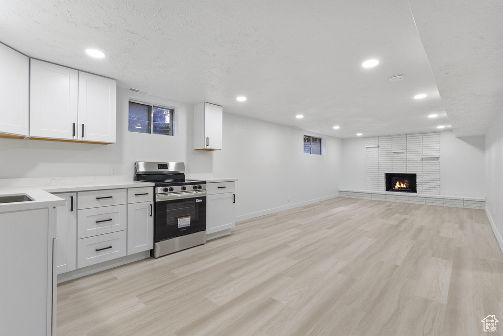 Kitchen featuring electric stove, white cabinets, light wood finished floors, light countertops, and a brick fireplace