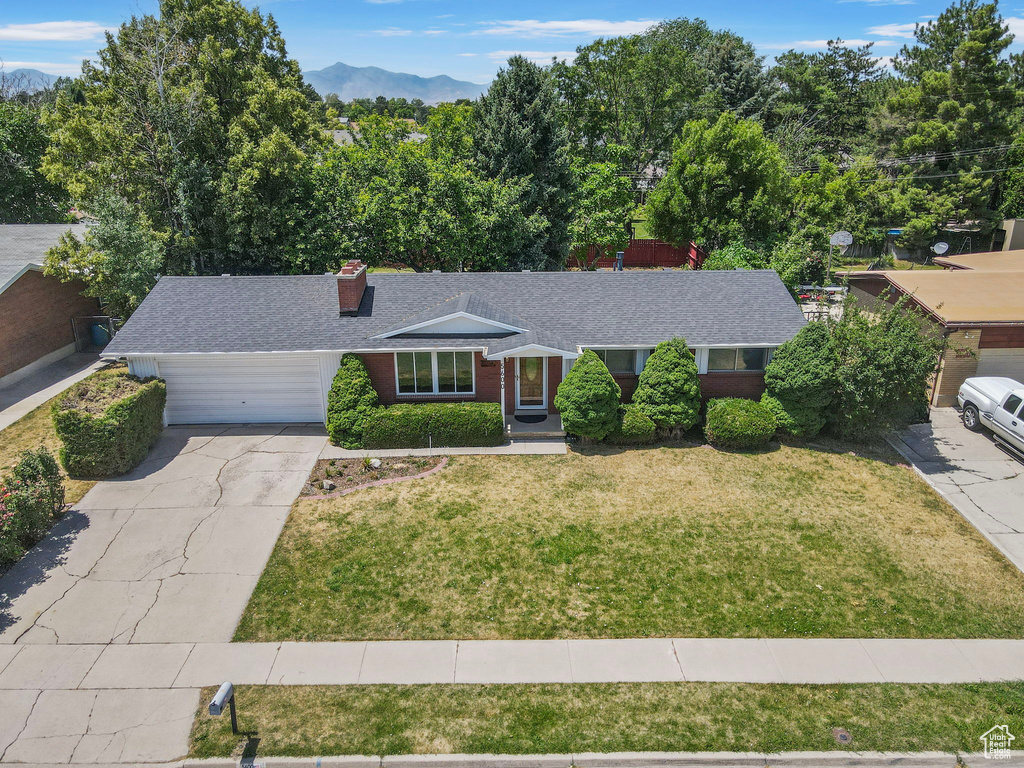 Ranch-style home with concrete driveway, brick siding, a garage, a front lawn, and a shingled roof