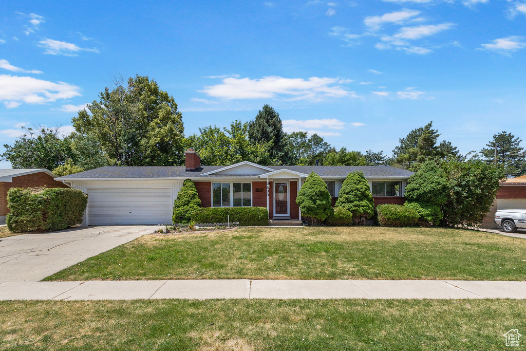 Single story home with an attached garage, driveway, a front yard, a chimney, and brick siding