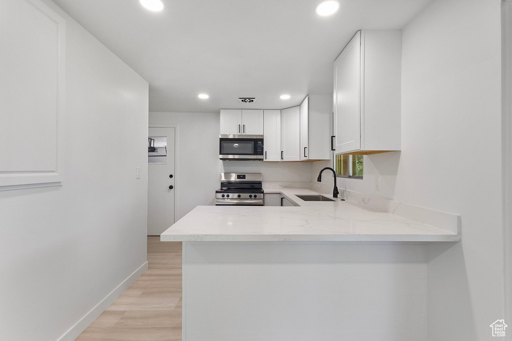 Kitchen featuring appliances with stainless steel finishes, recessed lighting, light stone countertops, white cabinetry, and light wood-style flooring