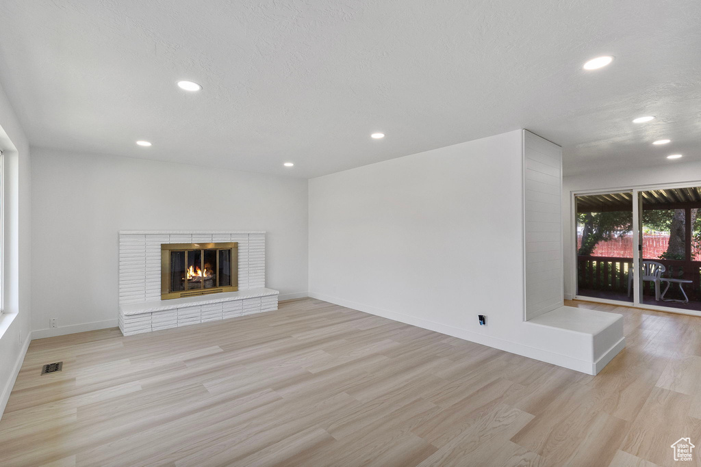 Unfurnished living room featuring recessed lighting, light wood-style floors, and a brick fireplace