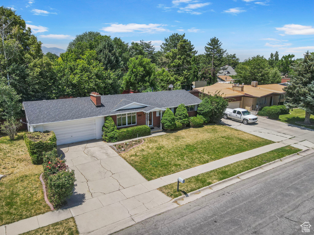 Ranch-style home with a garage, a chimney, roof with shingles, a front lawn, and concrete driveway