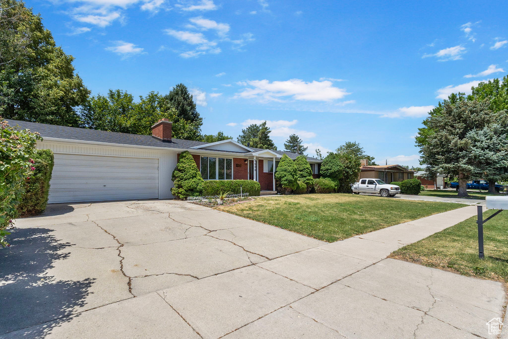 Ranch-style home with a front yard, a chimney, an attached garage, driveway, and brick siding