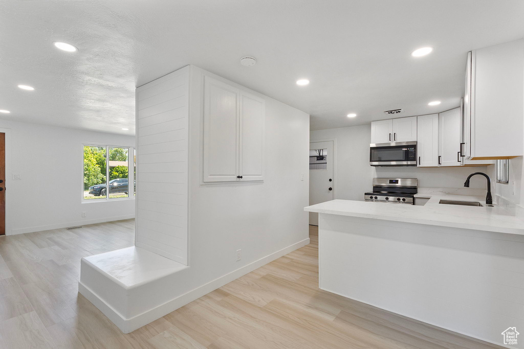 Kitchen featuring stainless steel appliances, recessed lighting, light countertops, white cabinetry, and light wood-type flooring