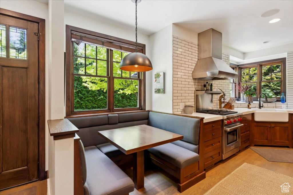Kitchen with breakfast area, island exhaust hood, premium stove, light wood finished floors, and decorative backsplash