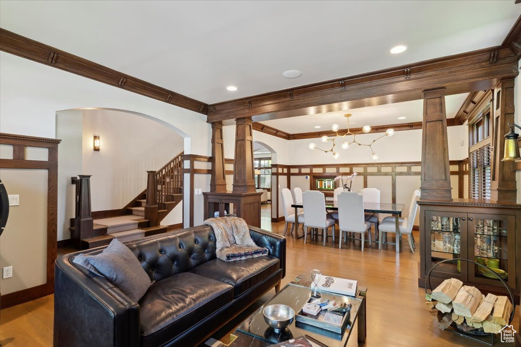 Living area featuring ornate columns, ornamental molding, arched walkways, stairs, and wood finished floors