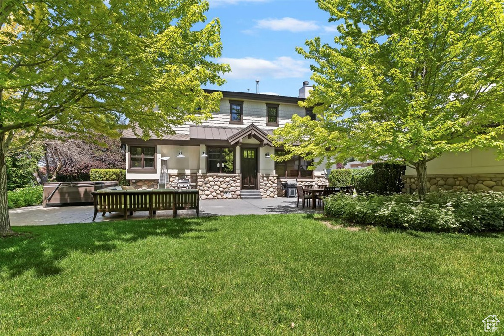 Rear view of house featuring stone siding, a patio, a lawn, and a chimney