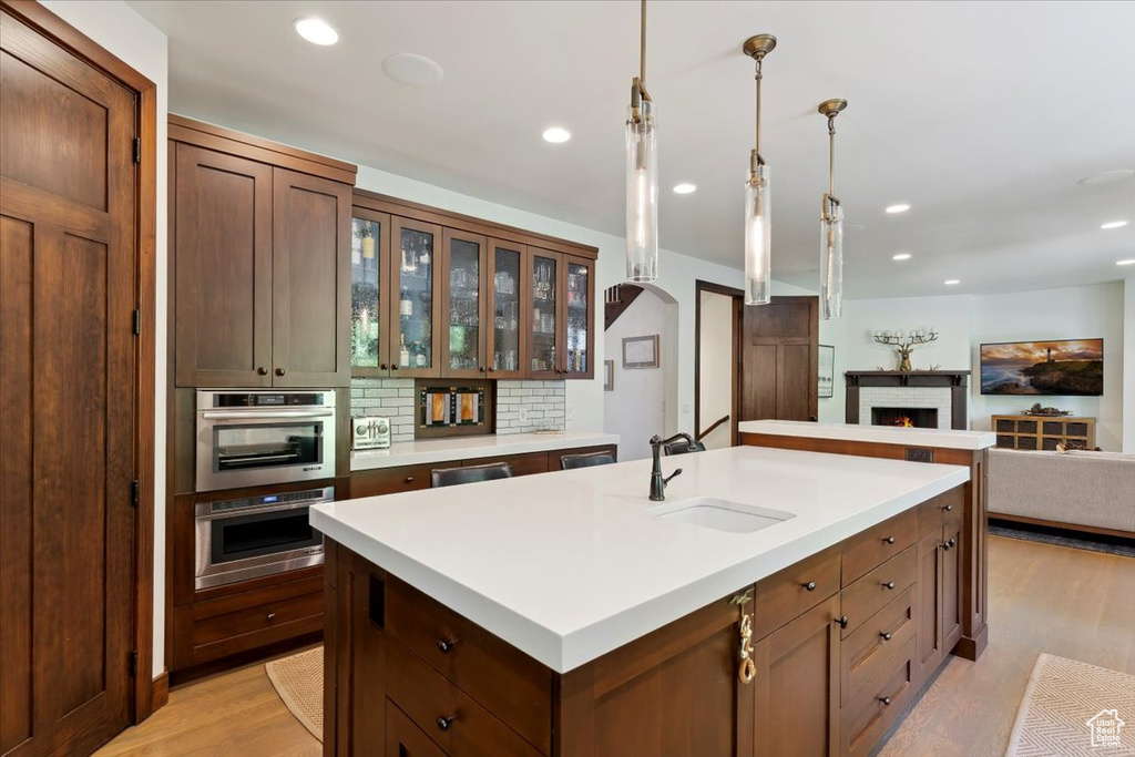 Kitchen with a center island with sink, light wood-type flooring, light countertops, decorative backsplash, and recessed lighting