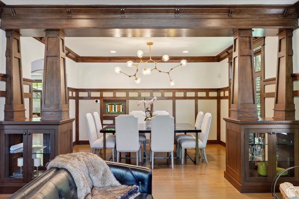 Dining area featuring decorative columns, wood finished floors, a chandelier, and ornamental molding