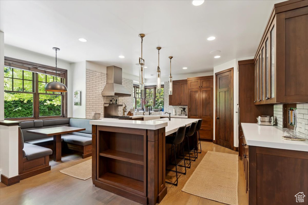 Kitchen with wall chimney exhaust hood, tasteful backsplash, light countertops, light wood-style flooring, and recessed lighting