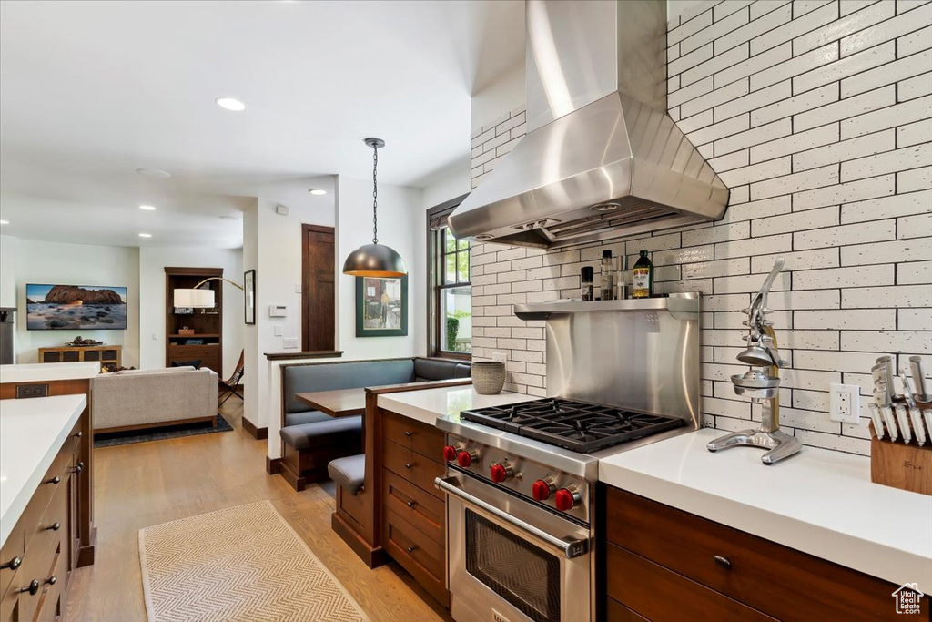 Kitchen with island range hood, premium range, light countertops, backsplash, and light wood finished floors