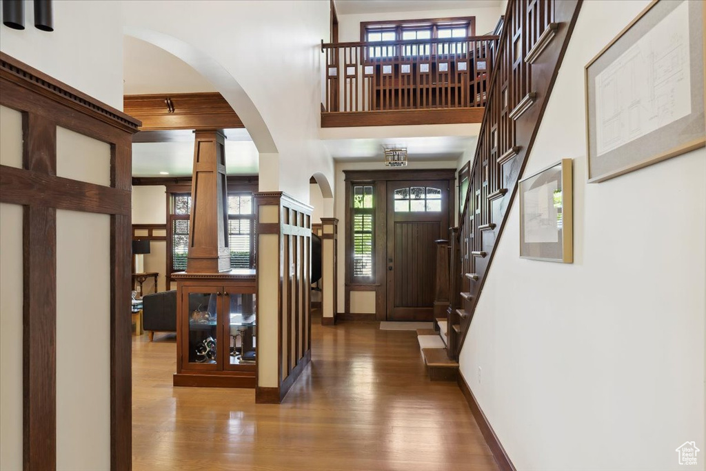 Foyer entrance with wood finished floors, arched walkways, ornate columns, a towering ceiling, and stairway