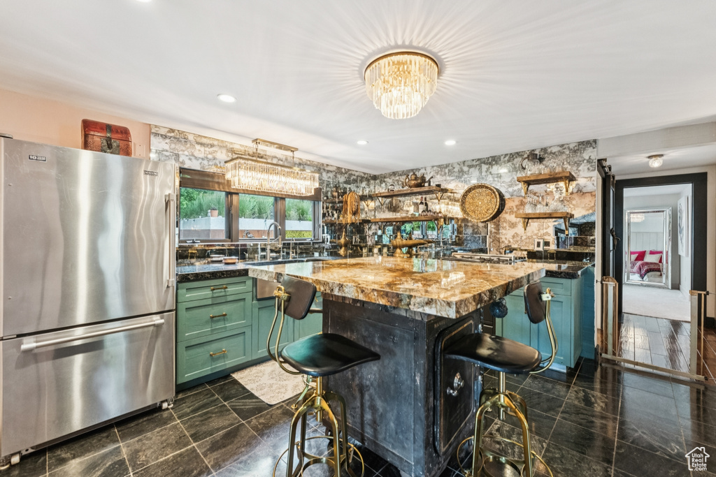 Kitchen with freestanding refrigerator, green cabinets, open shelves, a chandelier, and a kitchen bar