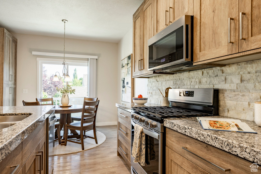 Kitchen featuring stainless steel appliances, decorative backsplash, light wood finished floors, light stone countertops, and hanging light fixtures