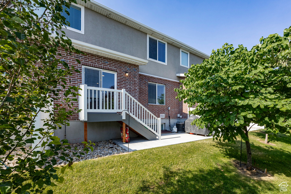 Rear view of house featuring brick siding, a lawn, a patio, and stucco siding