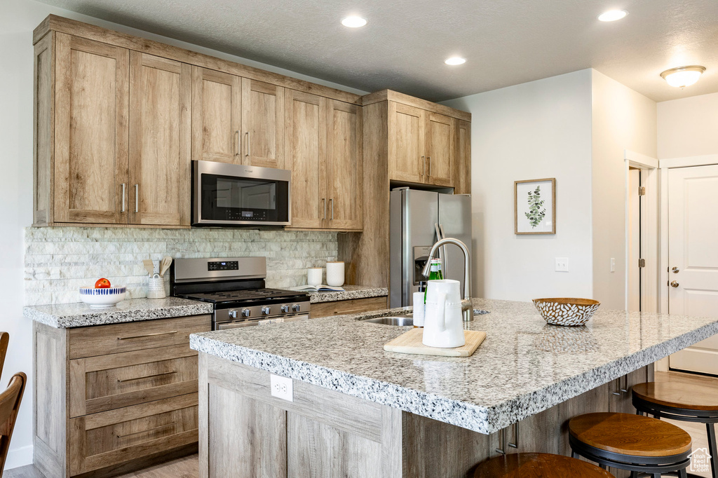 Kitchen featuring stainless steel appliances, a breakfast bar, backsplash, an island with sink, and recessed lighting