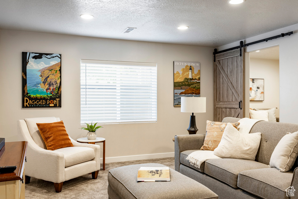 Living room with a barn door, light carpet, recessed lighting, and a textured ceiling