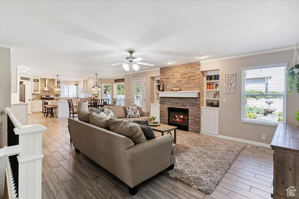Living room featuring wood finished floors, crown molding, a fireplace, ceiling fan, and recessed lighting