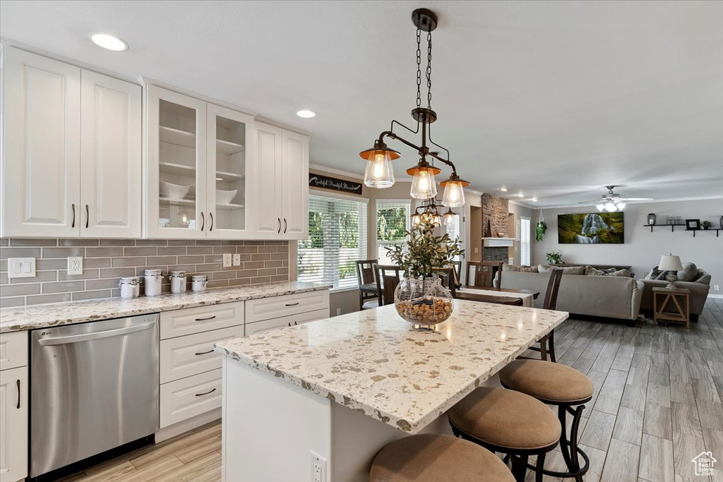 Kitchen with stainless steel dishwasher, a breakfast bar area, white cabinets, light wood-style floors, and recessed lighting