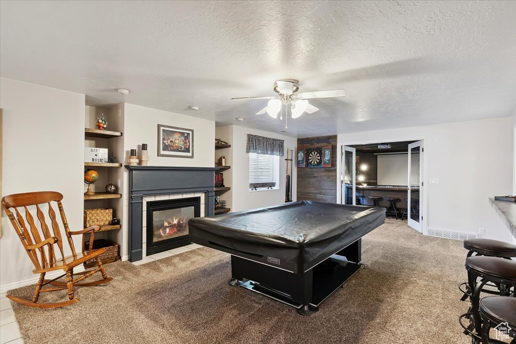 Rec room with pool table, a tiled fireplace, a ceiling fan, a textured ceiling, and carpet floors