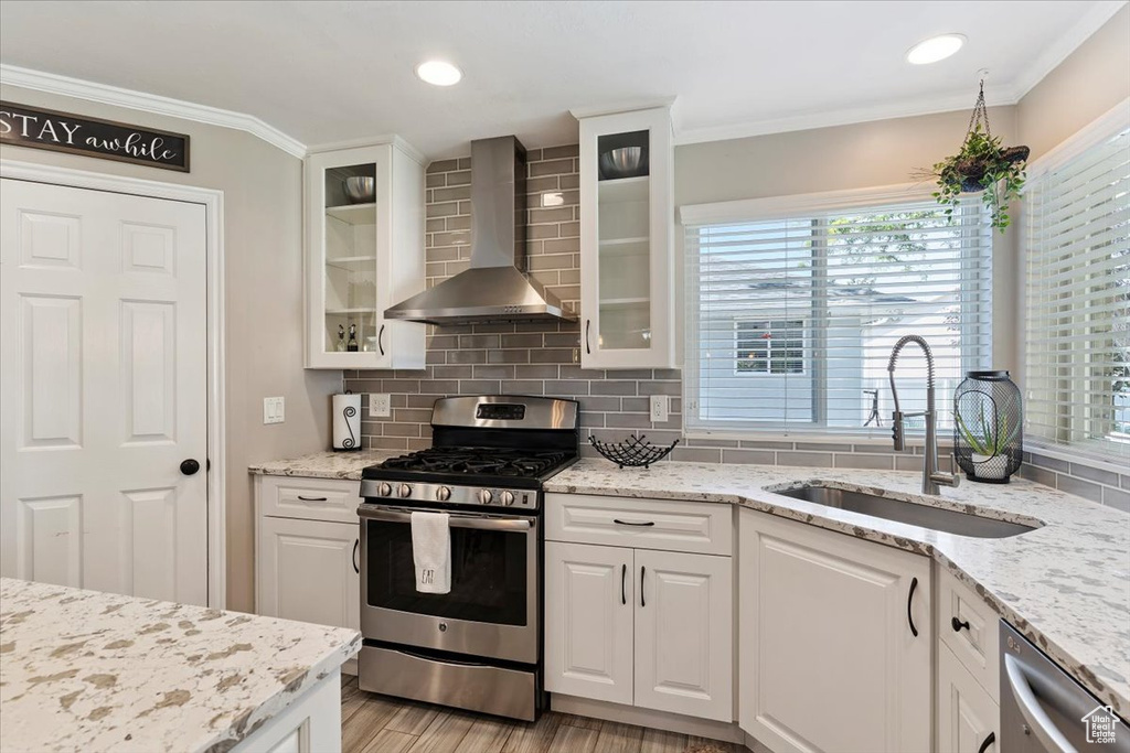 Kitchen with stainless steel appliances, wall chimney exhaust hood, light wood-style floors, decorative backsplash, and white cabinetry