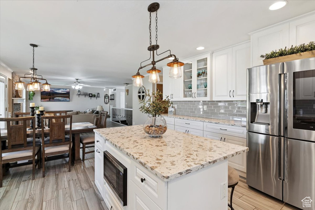 Kitchen featuring appliances with stainless steel finishes, backsplash, a kitchen island, glass insert cabinets, and white cabinetry