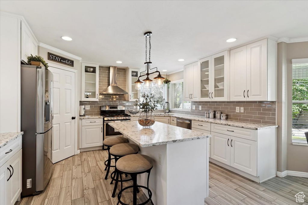 Kitchen with appliances with stainless steel finishes, wall chimney range hood, a kitchen breakfast bar, wood finish floors, and ornamental molding