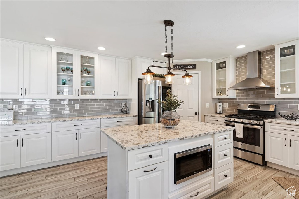 Kitchen with stainless steel appliances, wall chimney range hood, backsplash, white cabinets, and recessed lighting