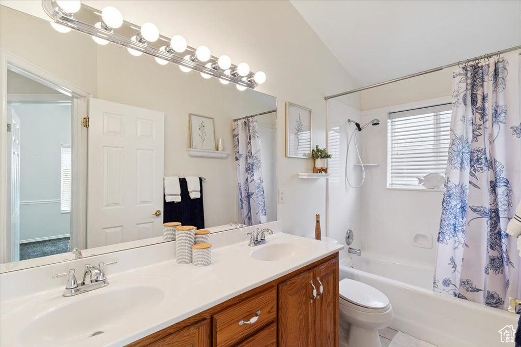 Bathroom featuring vaulted ceiling, shower / bath combination with curtain, and double vanity