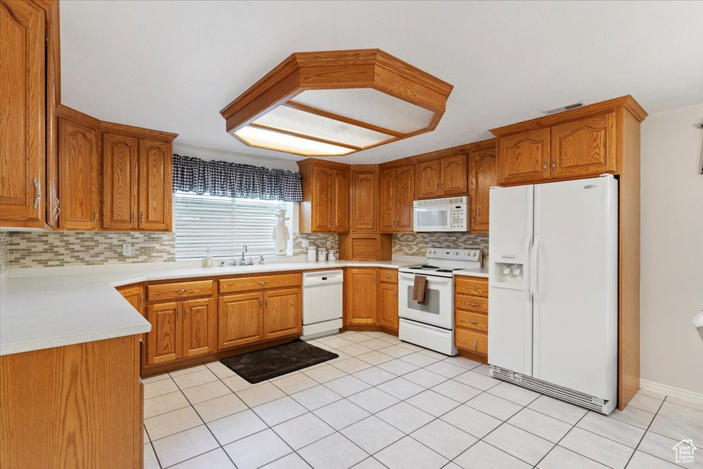 Kitchen with white appliances, tasteful backsplash, light countertops, brown cabinets, and light tile patterned flooring