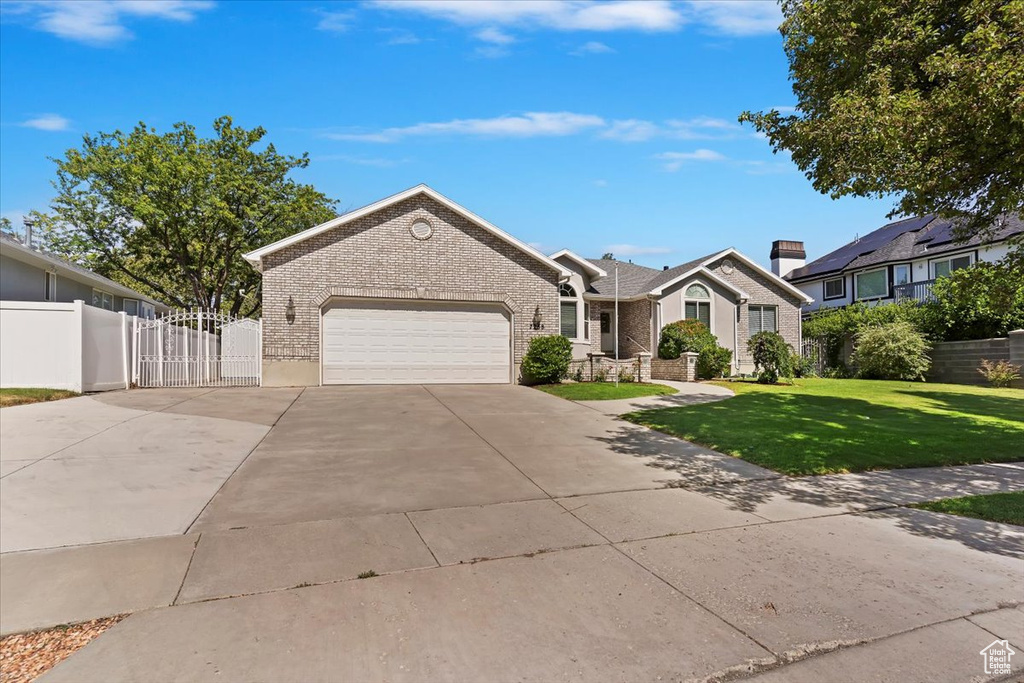 Ranch-style home featuring an attached garage, brick siding, driveway, and a gate