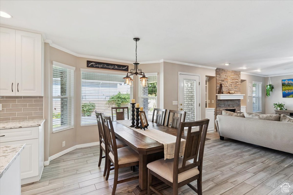 Dining room with a chandelier, crown molding, light wood-style flooring, a fireplace, and recessed lighting