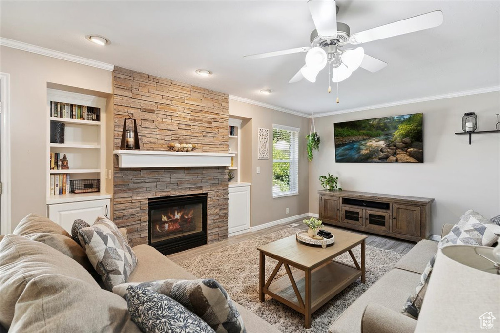 Living area featuring crown molding, wood finished floors, a stone fireplace, ceiling fan, and built in features