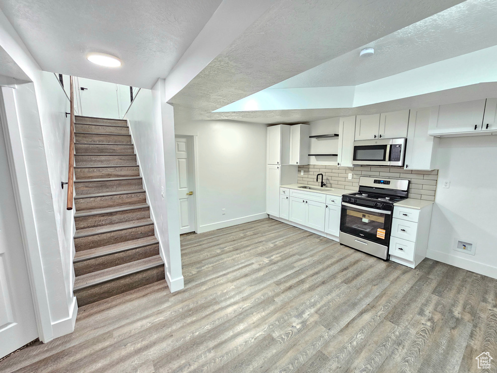 Kitchen with appliances with stainless steel finishes, light countertops, decorative backsplash, light wood-style flooring, and white cabinetry