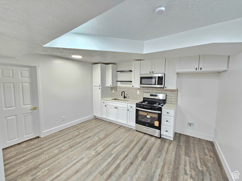 Kitchen with stainless steel appliances, a textured ceiling, light wood-style floors, tasteful backsplash, and light countertops