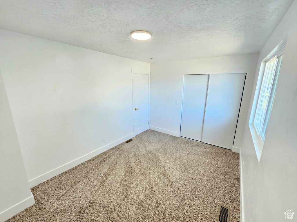 Unfurnished bedroom featuring light colored carpet, a textured ceiling, and a closet