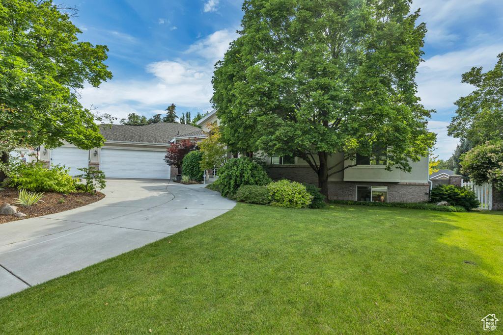 Obstructed view of property featuring driveway, an attached garage, a front yard, and brick siding