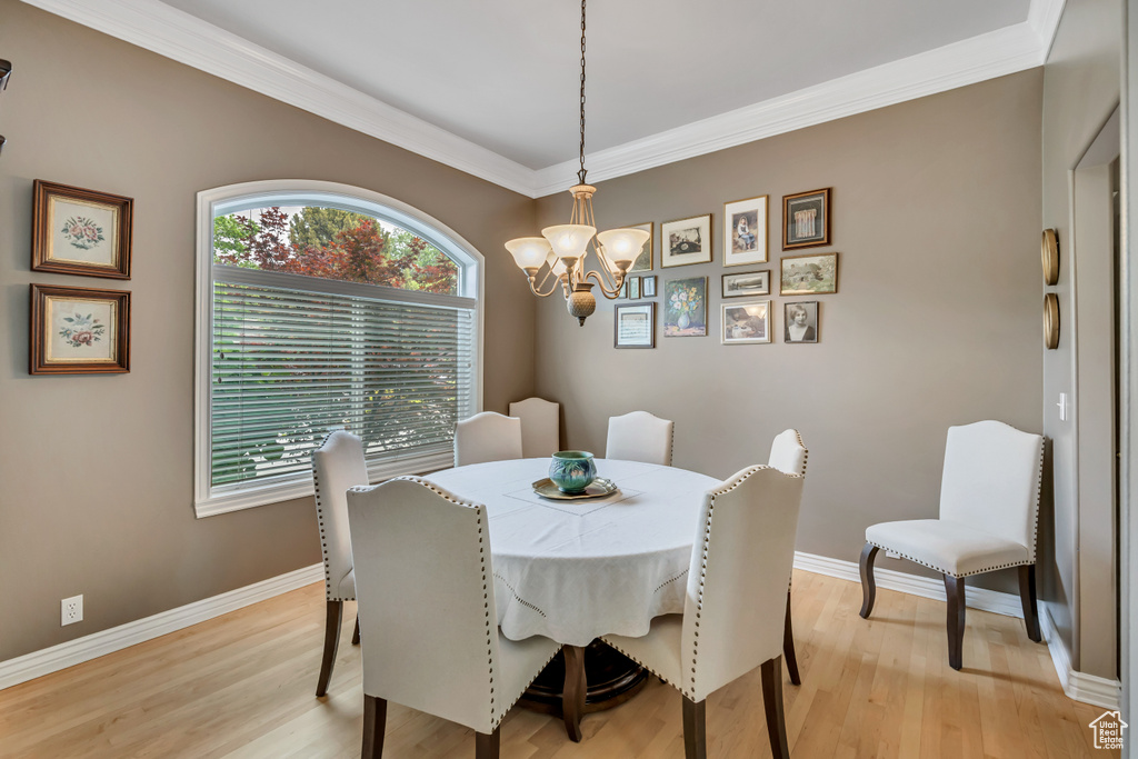Dining space with a chandelier, light wood-type flooring, and ornamental molding