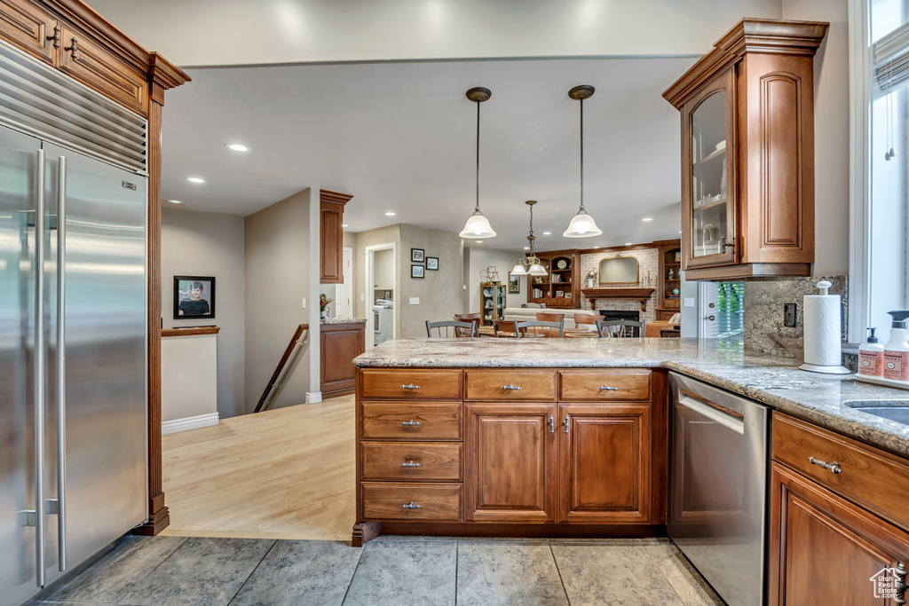 Kitchen with stainless steel appliances, brown cabinets, a peninsula, glass insert cabinets, and recessed lighting