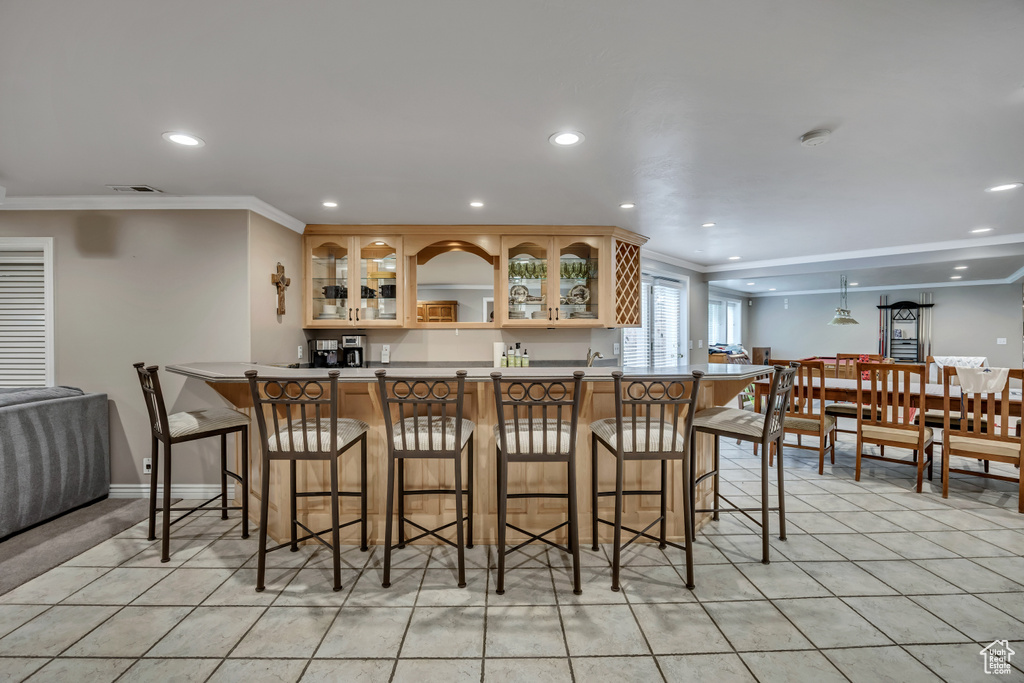Kitchen featuring recessed lighting, ornamental molding, a kitchen bar, glass insert cabinets, and light tile patterned floors