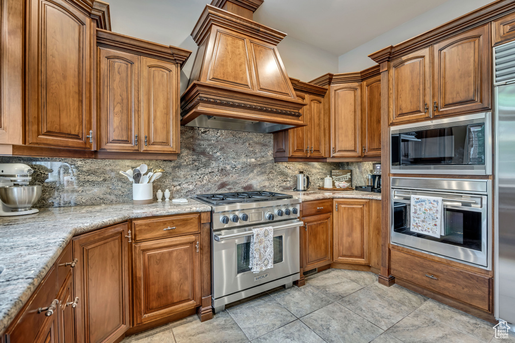 Kitchen featuring stainless steel appliances, custom exhaust hood, decorative backsplash, and brown cabinets