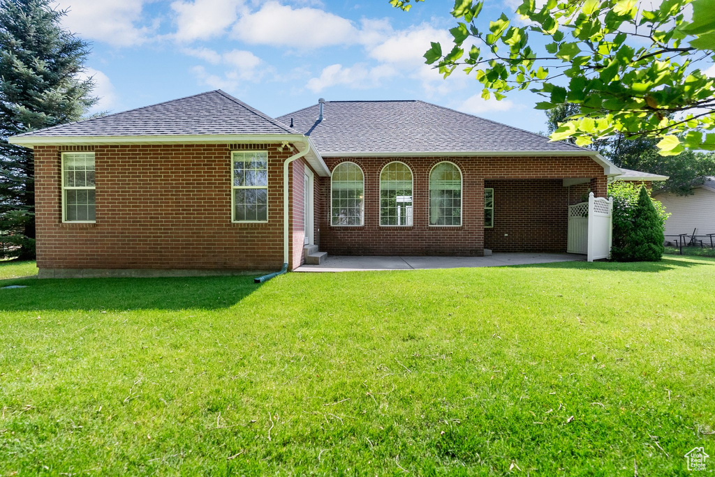 Back of house featuring a shingled roof, a patio area, a lawn, and brick siding