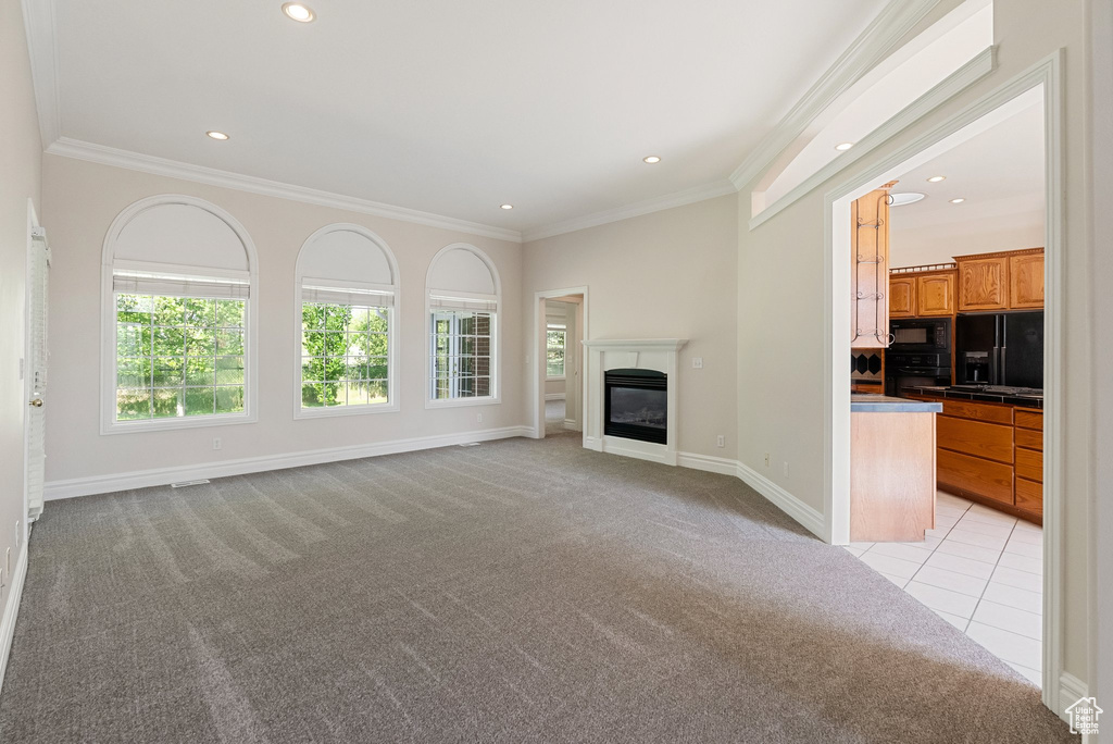 Unfurnished living room with light colored carpet, ornamental molding, recessed lighting, a glass covered fireplace, and light tile patterned flooring