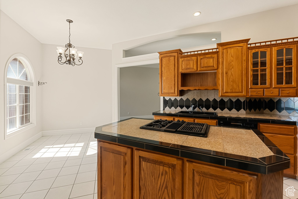 Kitchen featuring black gas cooktop, tasteful backsplash, light tile patterned floors, a chandelier, and a kitchen island