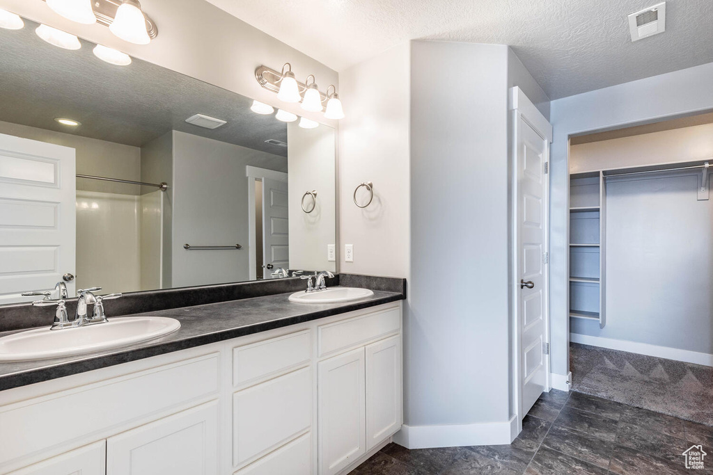 Bathroom with double vanity, a textured ceiling, a spacious closet, and a shower