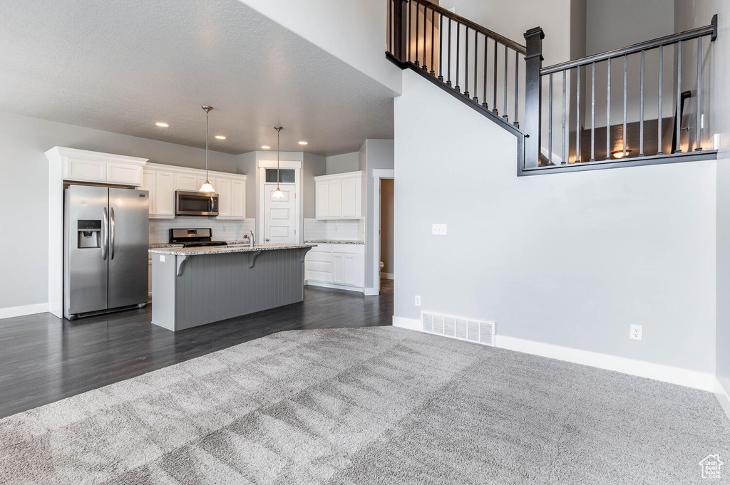 Kitchen featuring stainless steel appliances, white cabinets, a breakfast bar, a center island with sink, and light stone countertops