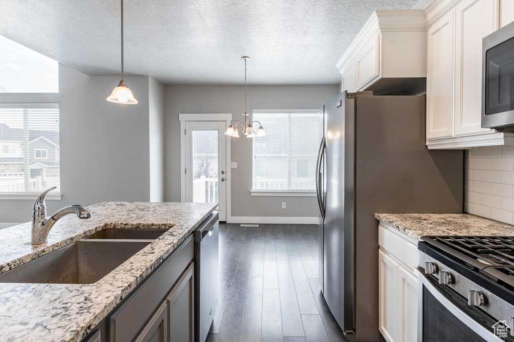 Kitchen with stainless steel appliances, dark wood-style flooring, white cabinetry, a chandelier, and decorative light fixtures