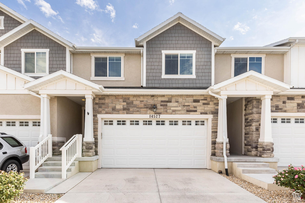 View of front of property featuring stone siding, an attached garage, concrete driveway, and stucco siding