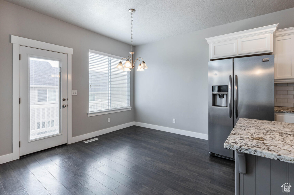 Kitchen featuring stainless steel fridge with ice dispenser, white cabinets, a chandelier, light stone countertops, and tasteful backsplash
