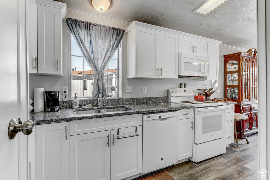 Kitchen with white appliances, wood finished floors, white cabinetry, a textured ceiling, and dark stone countertops